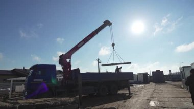 ALMATY, KAZAKHSTAN - 17 Ekim 2024: Crane inşaat alanındaki işçi kontrolündeki kamyon römorkuna plaka yüklüyor. İnşaat makinesi mavi gökyüzüne karşı ağır blokları kamyona taşıyor.