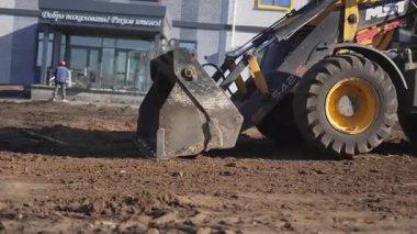ALMATY, KAZAKHSTAN - Nisan 04 2025: Modern buldozer şehir bloğunda kirli zemin boyunca geri dönüyor. Güneşli bir günde kentsel inşaat alanında kepçeli güçlü bir toprak taşıyıcı çalışıyor.