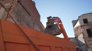 ALMATY, KAZAKHSTAN - Nisan 04 2025: Toprak taşıyıcı kova yıkım alanındaki kamyon römorkuna toprak döküyor. Kazıcı temiz enkaz yüklü kamyon açık mavi gökyüzüne karşı ağır çekim