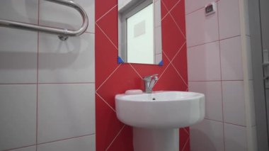 Seramik lavabo aynası ve krom havlu ısıtıcısı boş tuvalette. Modern ekipmanlar ve otel banyosunun beyaz ve kırmızı fayanslı duvarı.