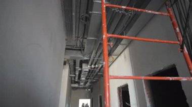 Bina tavanında elektrik kabloları olan kırmızı merdiven ve havalandırma kanalı. Tamamlanmamış endüstriyel bina iç görünümü