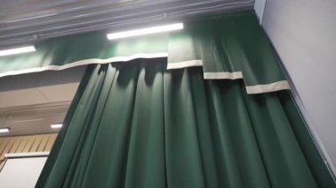 Dar LED lambalarla çerçevelenmiş ağır perdeler ahşap tavana yükselir. Sahne perdeleri yukarı doğru harmanlama dokusu yüksekliği ve ince ışık