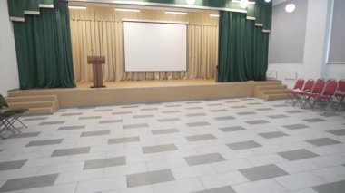 Sahne perdeleri açık, projektör arka planıyla birlikte etkinlik odası. Uzay sahne teknolojisi ve oturma düzenini işlevsel organize tasarım ile harmanlıyor