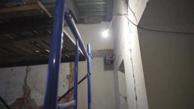 İnşaat iskeleleri alçıyla sıvanmış, loş ışıklı bir odada kablolarla duruyor. Kırılganlık eksikliği ve restorasyonun endüstriyel cazibesi