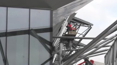 Asansör sepetindeki adam fayansları açısal yüzeye bağlıyor. Sivri kenarlı fütüristik duvarlar düzgün bir kaplama sağlar. Yüksek irtifa çalışması