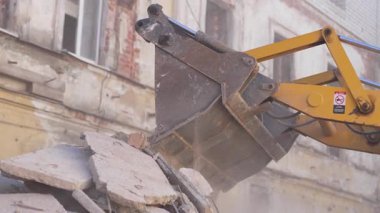 Büyük kazıcı kovası yıpranmış eski binanın yakınındaki ağır enkazı kırıyor. Makine, solup giden cephenin yakınındaki tuğla yığınlarını dikkatlice yırtıyor
