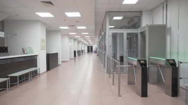 Hastane koridoru beyaz duvarlar ve parlak zeminle uzanıyor. Resepsiyon masası, teknik odalarla birlikte giriş kapılarının karşısında duruyor.