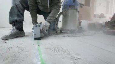 Bir adam beton zeminde duvar kovalayıcısıyla yer altı ısıtması kurmak için ara veriyor. Yakın plan.