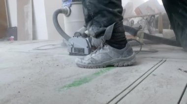 Bir adam beton zeminde duvar kovalayıcısıyla yer altı ısıtması kurmak için ara veriyor. Yakın plan. 4K filmi