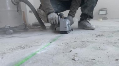 Bir adam beton zeminde duvar kovalayıcısıyla yer altı ısıtması kurmak için ara veriyor.