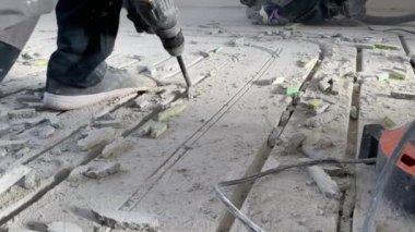Yakın plan. İnşaat sırasında bir işçi çekiçle beton döşemeyi kırıyor.
