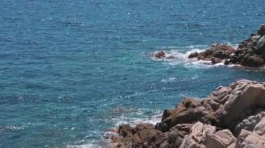 Dalgalar kayalık bir sahile çarpıyor. Kristal turkuaz renkli deniz manzaralı güzel bir deniz manzarası. 4K 
