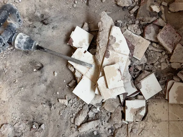 Seçici odaklanma. Bir kaya matkabı kırık seramik fayansların üzerinde yatar. İnşaat arkaplanı