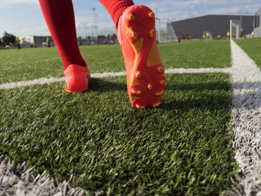 Kapatın. Futbol oyuncusu kırmızı krampon takıyor ve kavramak için küçük çiviler takıyor.