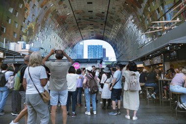 Rotterdam, Hollanda - 12 Temmuz 2025. Markthal Rotterdam 'ın içinde çeşitli yiyecek tezgahları, neon tabelaları ve kapalı alan pazarını keşfeden uluslararası ziyaretçilerle dolu canlı bir sahne..