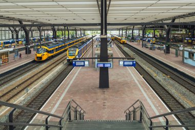 ROTTERDAM, NEtherlands, 1 Ağustos 2025. Hollanda 'da sarı ve mavi NS trenleri olan tren peronu ve arka planda kapalı terminali olan yolcular bekliyor.