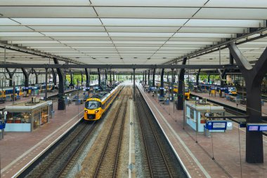 ROTTERDAM, NEtherlands, 1 Ağustos 2025. Hollanda 'da sarı ve mavi NS trenleri olan tren peronu ve arka planda kapalı terminali olan yolcular bekliyor.