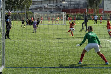 Rotterdam, Hollanda, 30 Ağustos 2025. Yeşil formalı genç futbolcu yeşil sahada takım arkadaşlarıyla yapılan bir futbol antrenmanı sırasında kurtarış antrenmanı yapıyor.