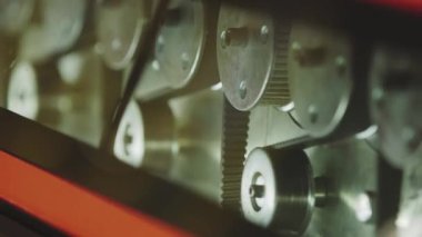 The glass enters the machine on rollers and undergoes a hardening process. The main gears that drive the machine rotate in the frame.