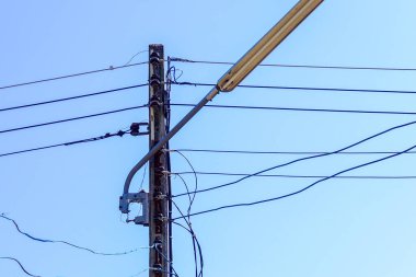 Elektrik kabloları ve elektrik kablolarıyla elektrik direği, mavi gökyüzü arka planında uzun beton sütunlarda sokak aydınlatması.
