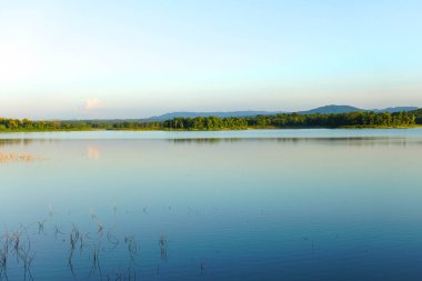 Gün batımında berrak mavi gökyüzü altında orman ve dağ yansıması ile sakin göl