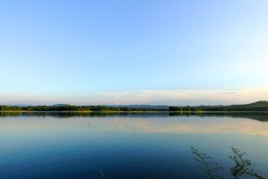 Gün batımında berrak mavi gökyüzü altında orman ve dağ yansıması ile sakin göl