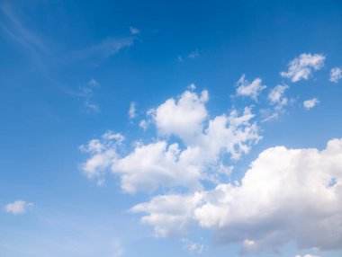 Pofuduk beyaz bulutlu, parlak bir günde, engin mavi bir gökyüzü. Yumuşak, beyaz bulutlarla dolu sakin mavi gökyüzü huzurlu ve geniş bir doğal manzara yaratıyor..