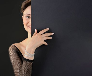 smiling beautiful girl on dark background, pointing with her hand at billboard