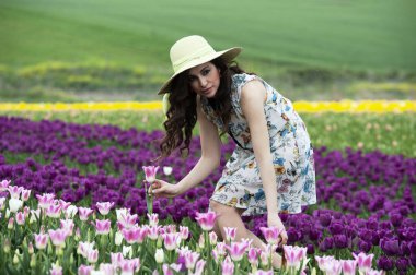 Şapkalı, beyaz elbiseli, tarlada bir buket çiçekli güzel bir kadın.