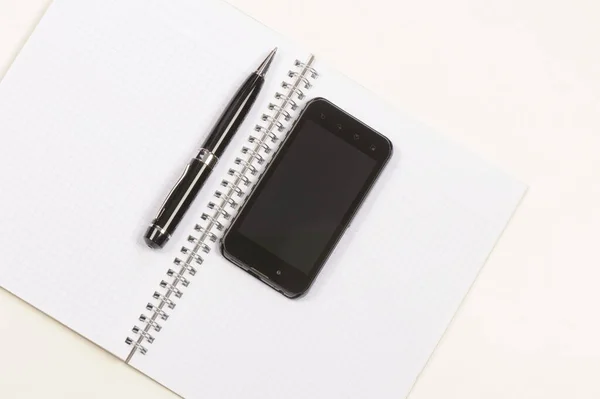 白い木製の背景にペンと携帯電話を持つ黒いスマートフォン — ストック写真