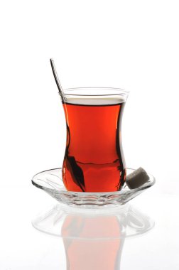 Cam bir tabakta klasik Türk çay bardağı ve beyaz zemin üzerinde şeker küpleri.