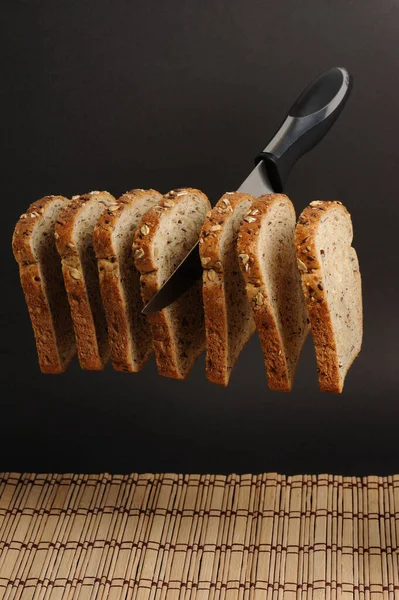 Siyah zemin üzerinde çoklu tahıllı ekmek havasını dilimleyen bıçak.