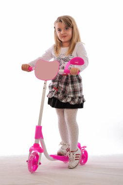 Beyaz arka planda pembe scooter 'ı olan küçük tatlı bir kız.