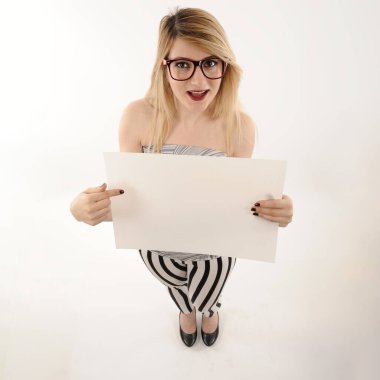 Sarışın ve gözlüklü güzel bir kız beyaz arka planda mesaj alanı olan beyaz boş bir afiş tutuyor.