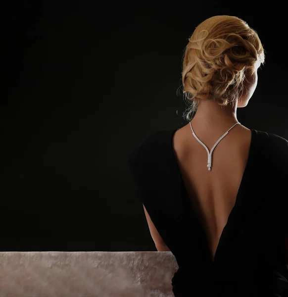 漂亮的金发女人背着钻石项链 从后面看去 她穿着一件黑色底色的低胸黑色连衣裙 — 图库照片