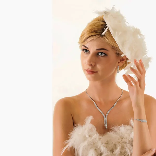 年轻美丽的金发女子 身穿白色羽衣 头戴一顶白色背景的钻石项链和手镯的帽子 — 图库照片