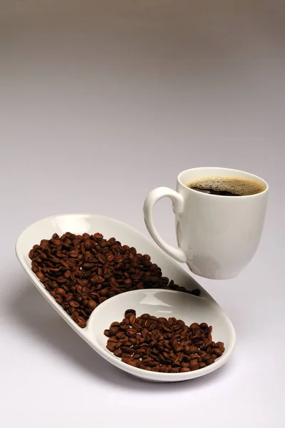 cup of coffee in a white ceramic cups on a saucer, close-up on a white background with coffee grains