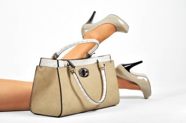 Siyah deri çantalı kadın bacakları ve beyaz arka planda ayakkabılar.