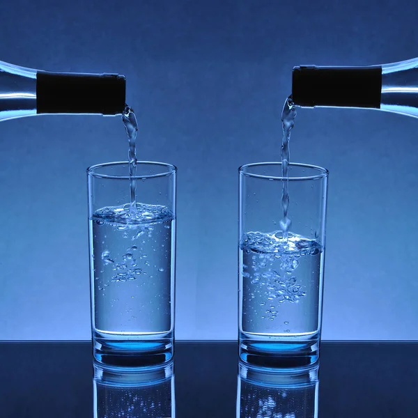 water glasses filling up with water flowing from the bottle mouth on a blue background