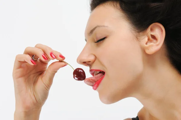 Beyaz arka planda kırmızı kiraz yiyen genç bir kadın.