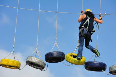 Kız, arka planda bulutlu ve mavi gökyüzü ile tırmanış ve hava yürüyüşü için renkli araba lastikleri üzerinde yürüyor ve egzersiz yapıyor.
