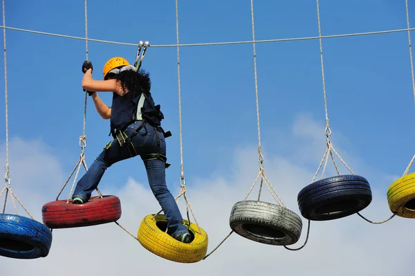 Kız, arka planda bulutlu ve mavi gökyüzü ile tırmanış ve hava yürüyüşü için renkli araba lastikleri üzerinde yürüyor ve egzersiz yapıyor.