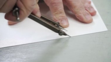 Beyaz bir kağıt parçasına pusula çizen bir adamın el resmi. Teknik çizim, mühendislik, tasarım, eğitim ve DIY projelerine odaklı videolar için ideal. Bu görüntü