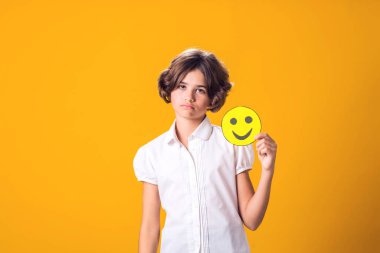 Upset girl holds happy emoticon. Stress and psychology concept clipart