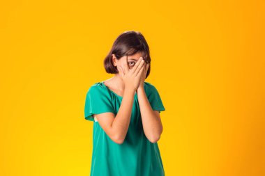 Korkmuş bir çocuk, sarı arka planda elleri ile gözlerini kapatmış. Hayal kırıklığı konsepti