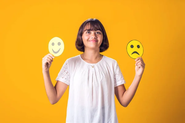 Girl holds sad and happy emoticons in hands. Mental health, psychology and children\'s emotions concept