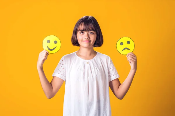 Girl holds sad and happy emoticons in hands. Mental health, psychology and children's emotions concept