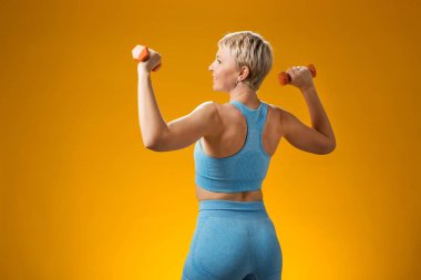 Sarı arka planda izole edilmiş, kısa sarı saçlı spor salonu kadını. Etkinlik ve sağlık konsepti