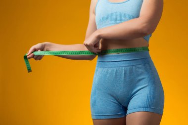 Sarı arka planda izole edilmiş mezuralı fitness kadını. Kilo kaybı ve sağlık konsepti