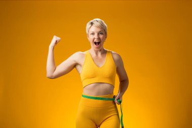 Sarı arka planda kısa saçlı, mezuralı bir kadın. Kilo kaybı ve sağlık konsepti